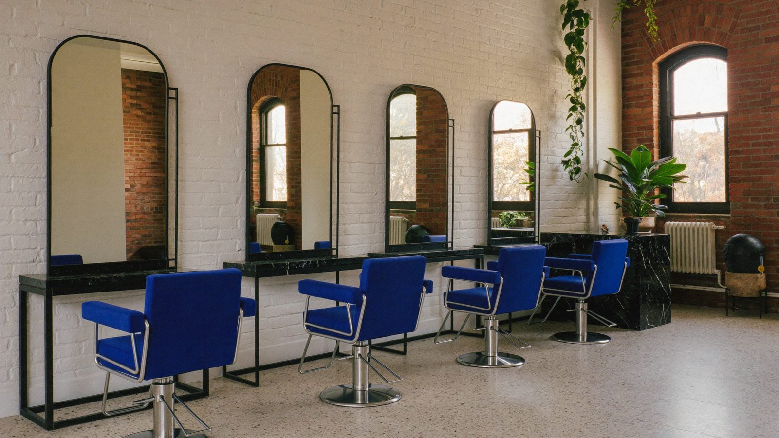 The salon at Glossary: whitewashed brick, arched windows, tall arched black mirrors and cobalt velvet chairs