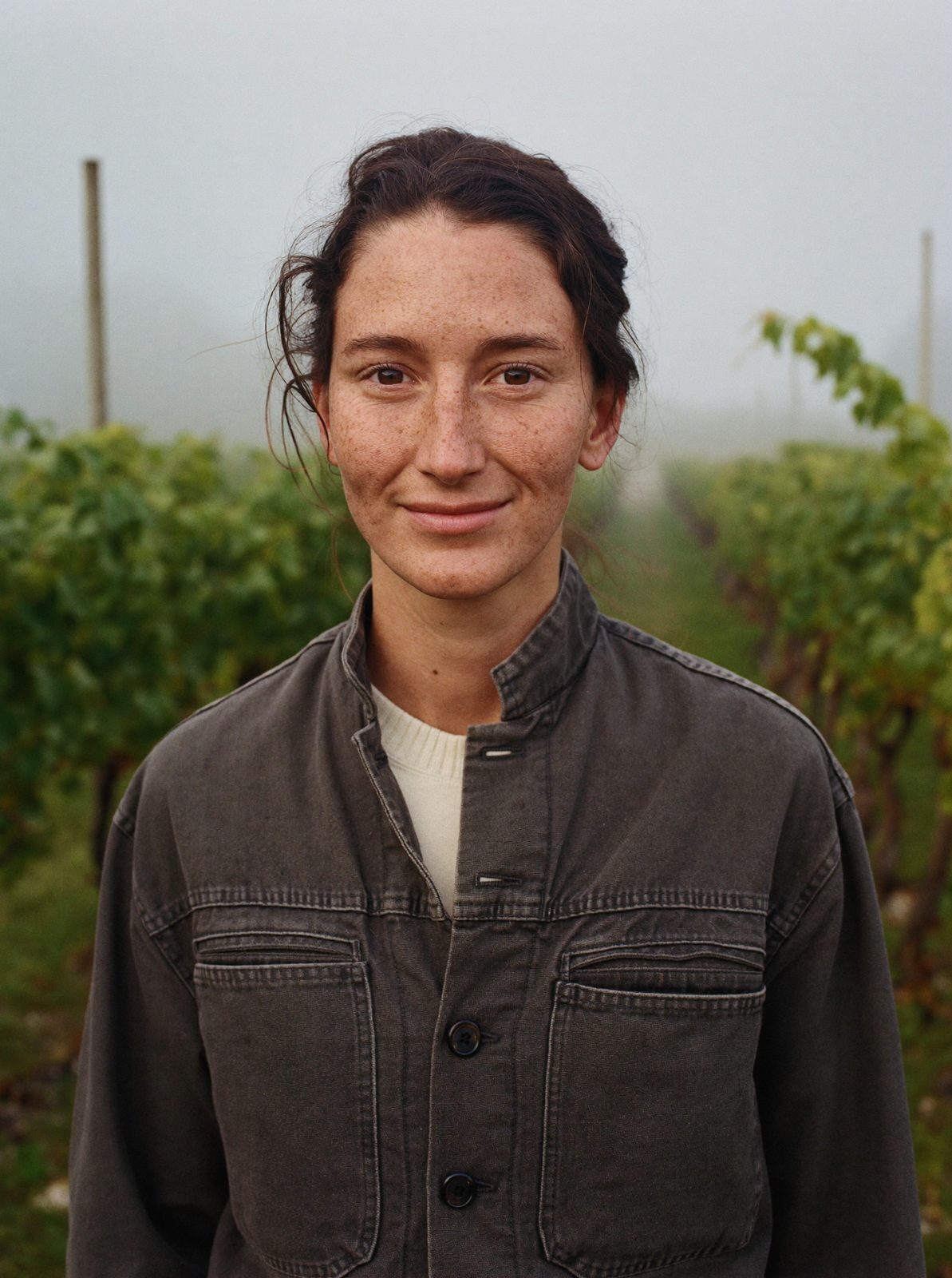 Mara Ellison standing between vine rows in the fog
