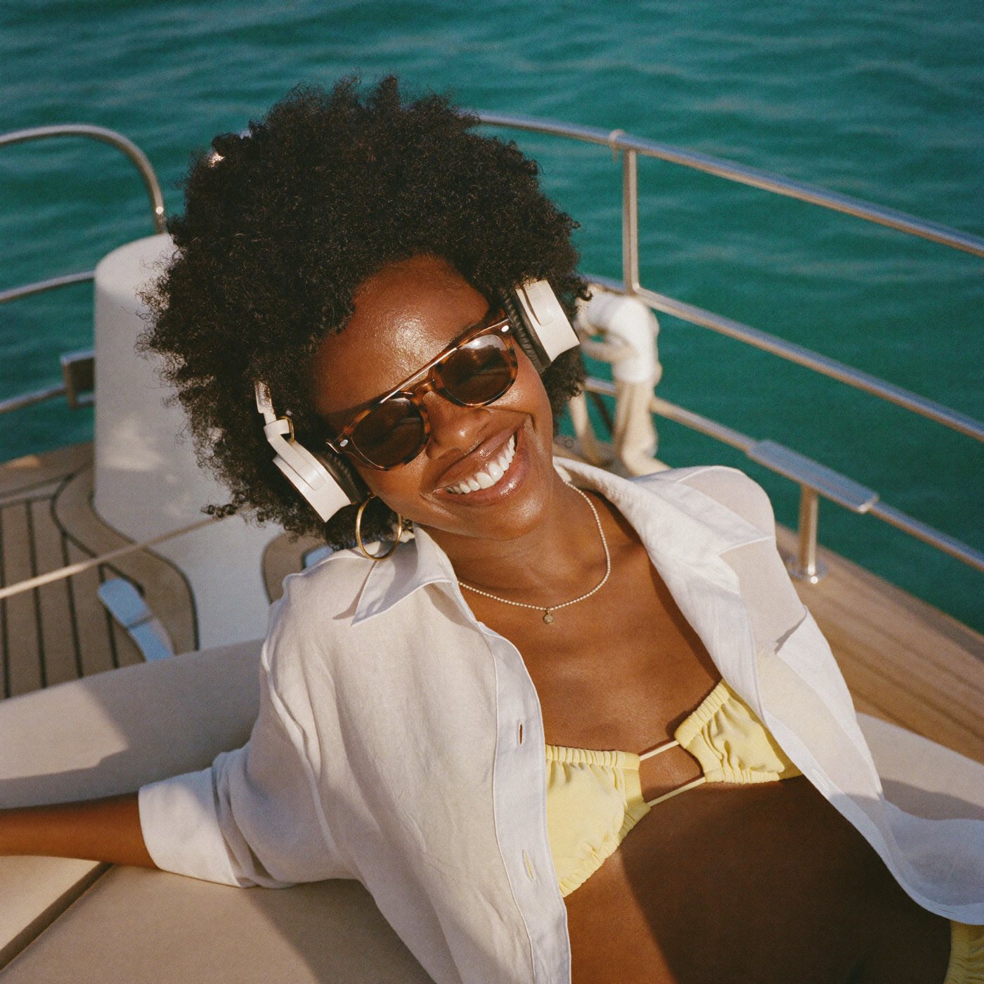 Woman in headphones and sunglasses laughing on a yacht deck in Mykonos