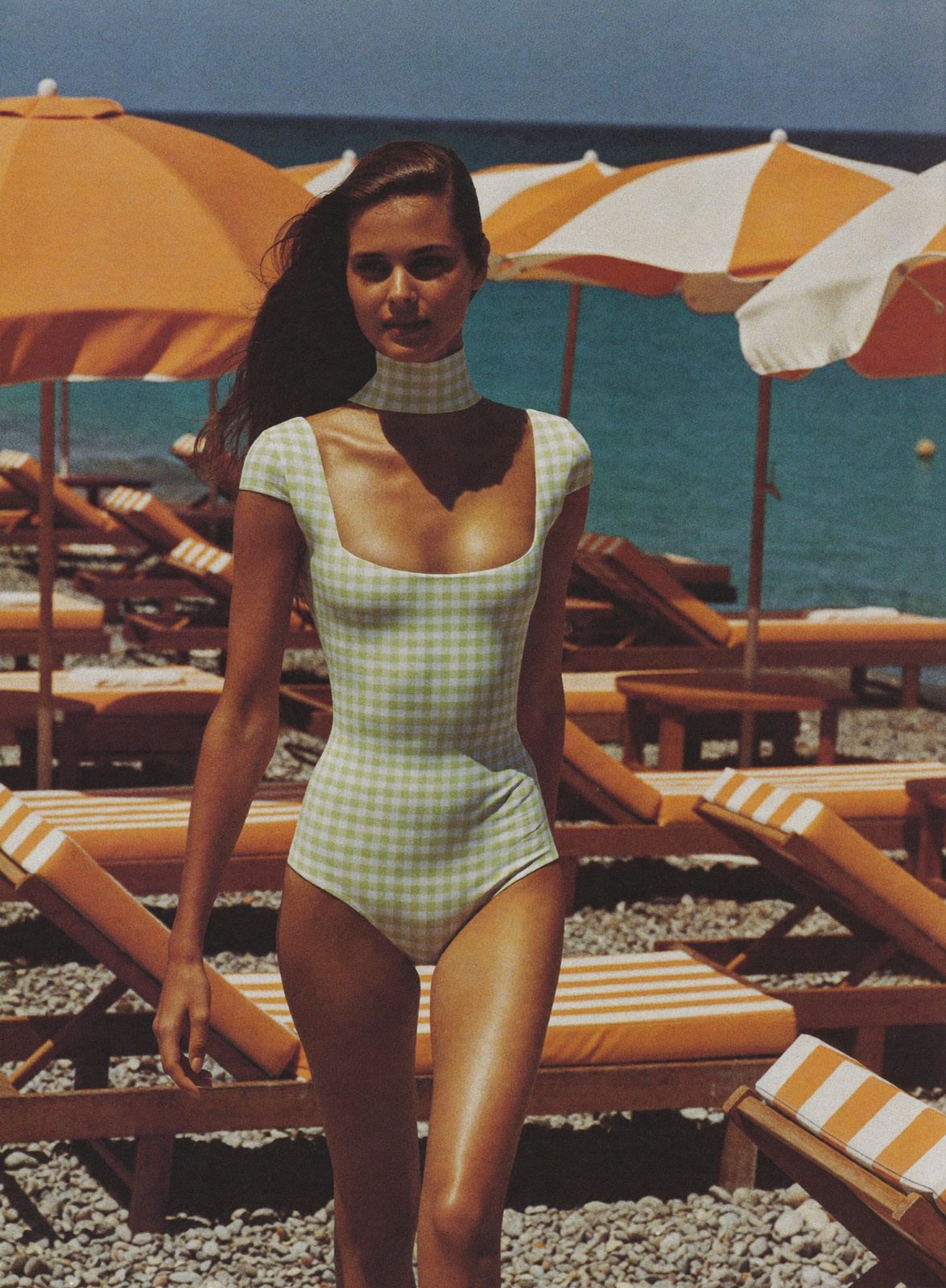 Model in The Cabana gingham one-piece at a beach club with striped umbrellas
