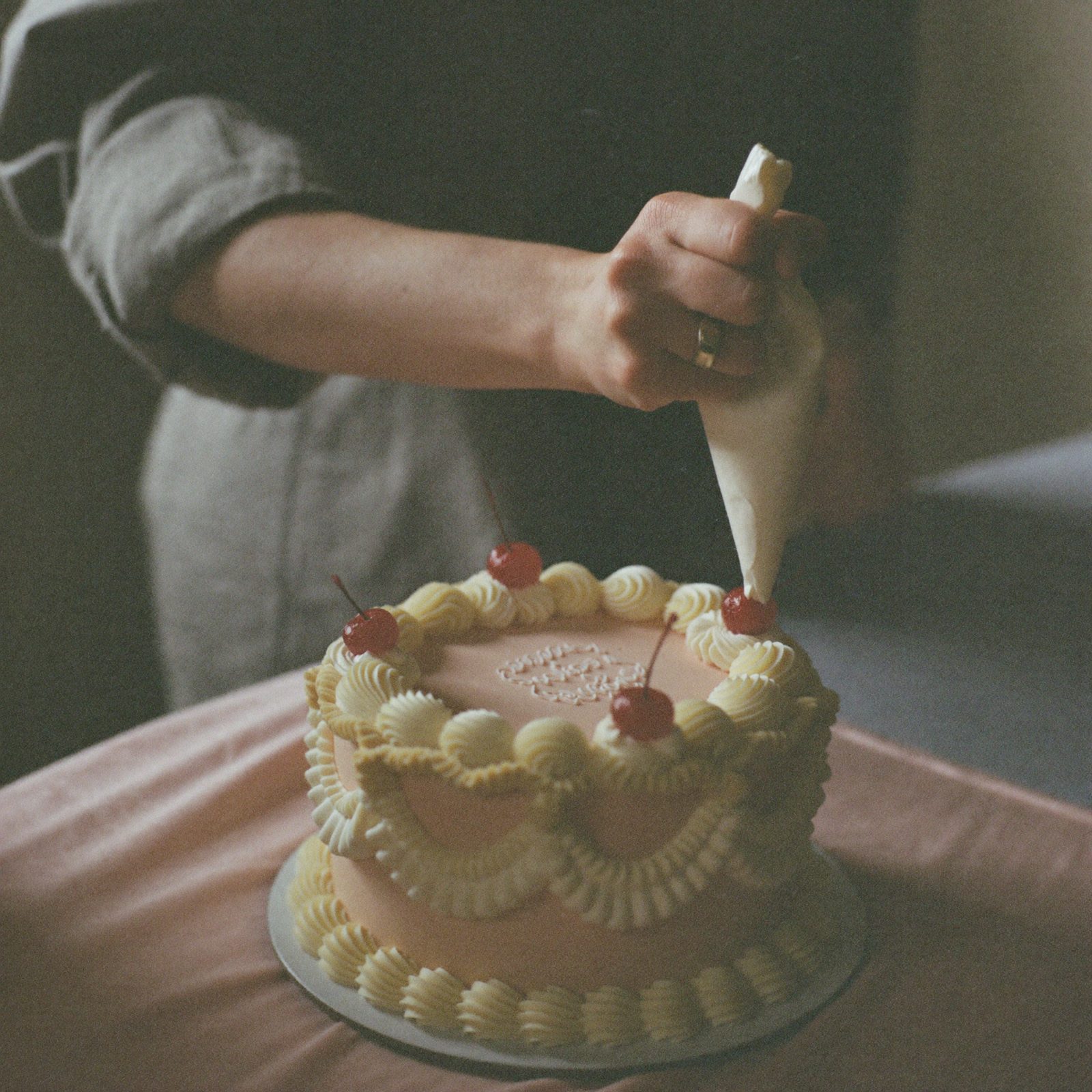 Hands piping buttercream scallops onto a blush cake
