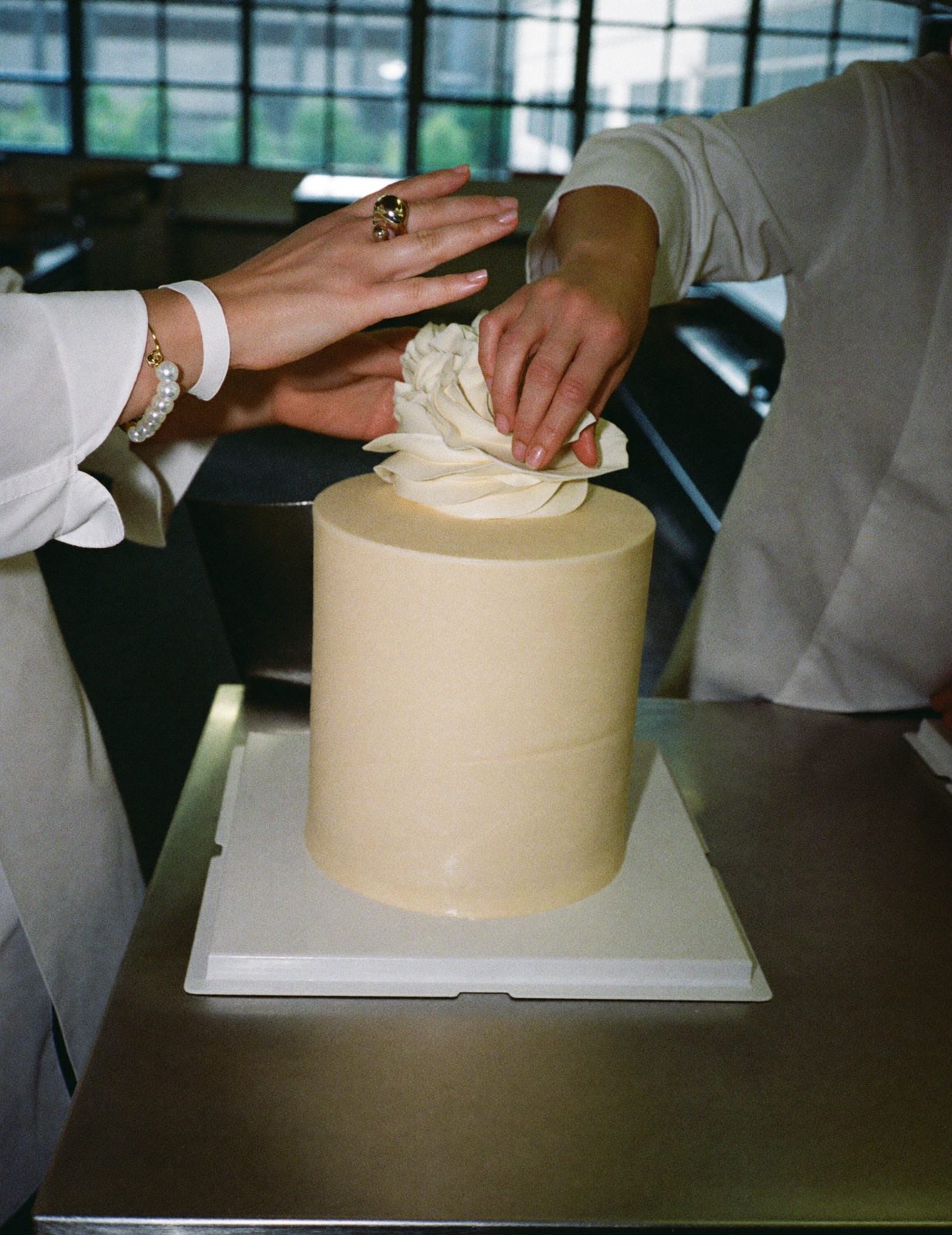Two pairs of hands placing a sugar peony on the top tier of an ivory cake